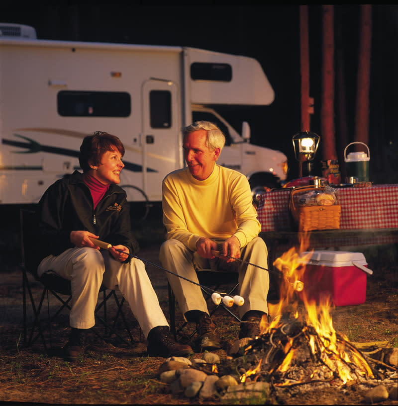 couple roasting marshmallows on a campfire beside their RV