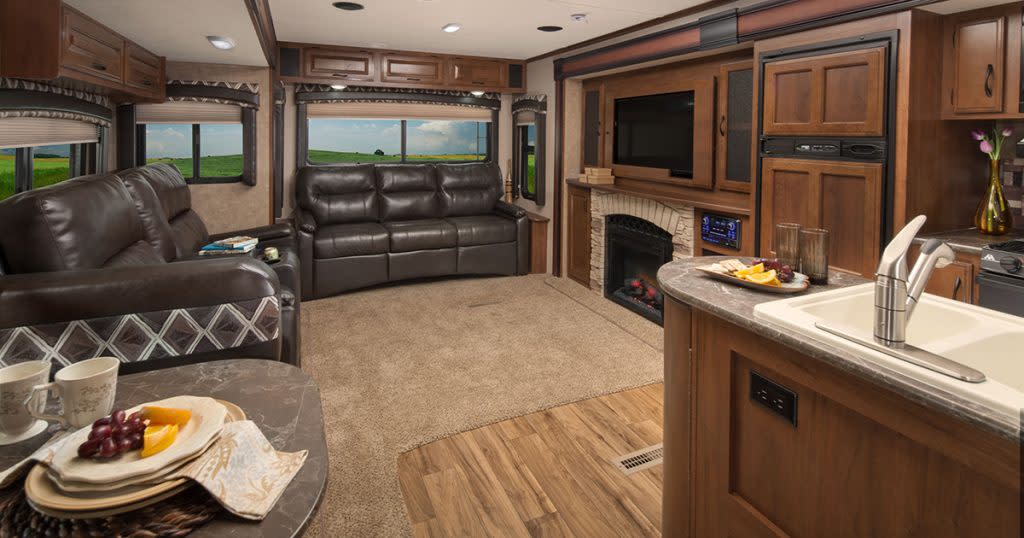 Fully- furnished RV interior with leather couches, kitchen area, and a fireplace