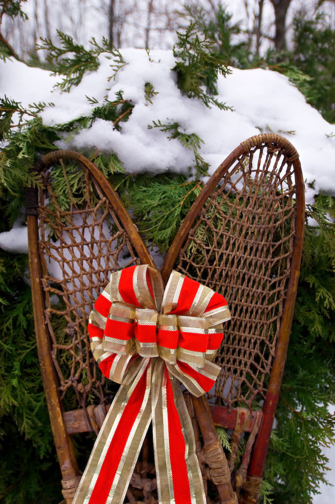 A pair of old wooden snowshoes are adorned with a ribbon as they rest against a cedar shrub in the snow in central Wisconsin during the Christmas holiday.