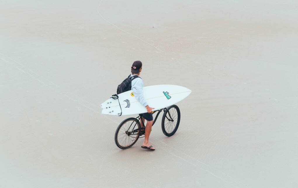 A man carries a surfboard on a bike in Daytona Beach.