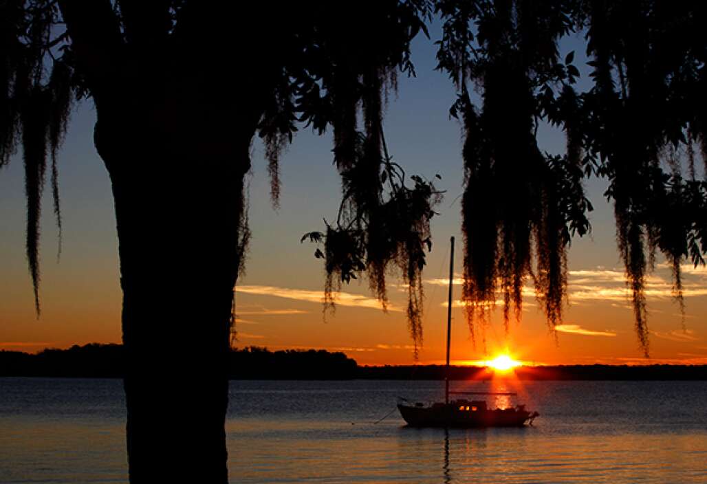 The rising sun shining as a cabin sailboat sails in the waters of the St. Johns River