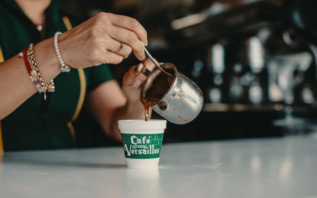 woman pouring coffee in a green cup from cafe versailles