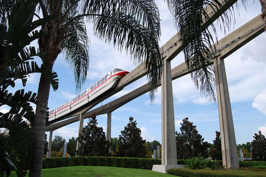 the disney world park monorail train gliding along the tracks next to palm trees