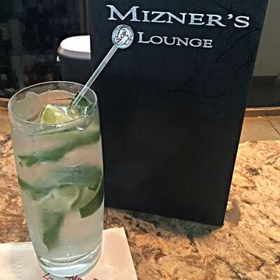 a bar menu that reads mizner's lounge sitting next to a mojito cocktail with stirrer