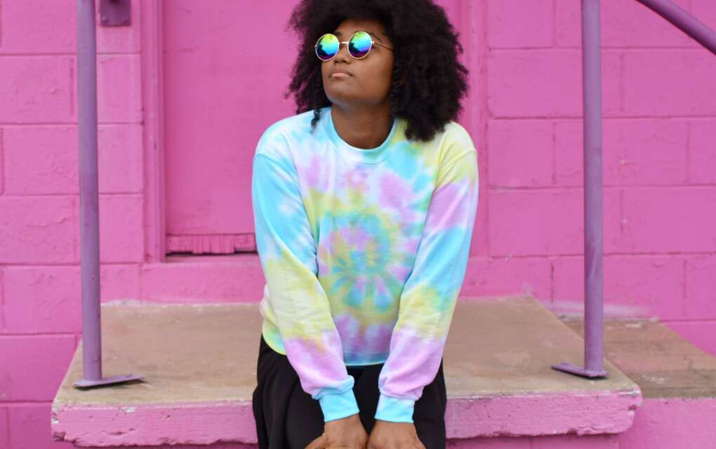 A Black womanl wearing sunglasses and colorful clothes with a pink wall in the background from The Fuzzy Pineapple, a black-owned business in Tallahassee, Fla.