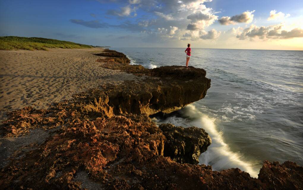 Woman standing on rock formation at Blowing Rocks Beach