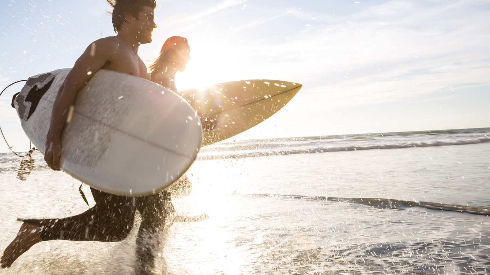 A couple running in the water holding their surfboard