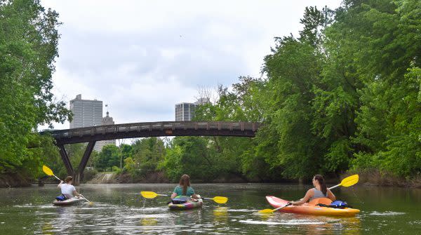 Three women kayaking on the St. Marys River in Fort Wayne, Indiana with the downtown skyline in the background