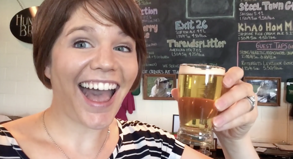 a smiling woman holds aloft a glass of beer