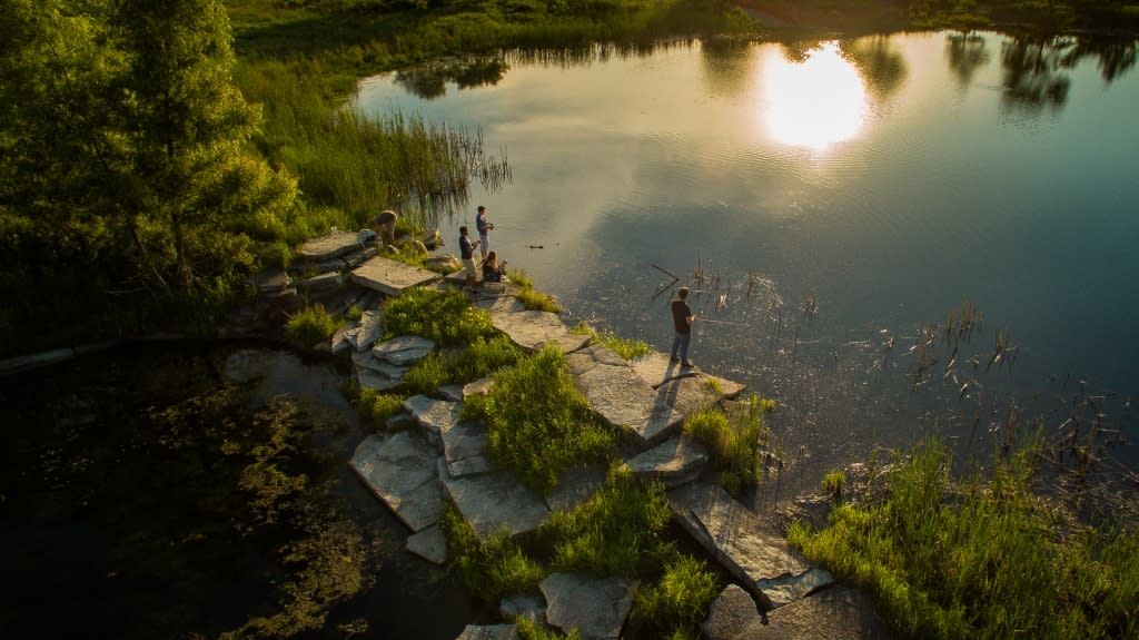 People fishing in a pond while standing on rock landscaping