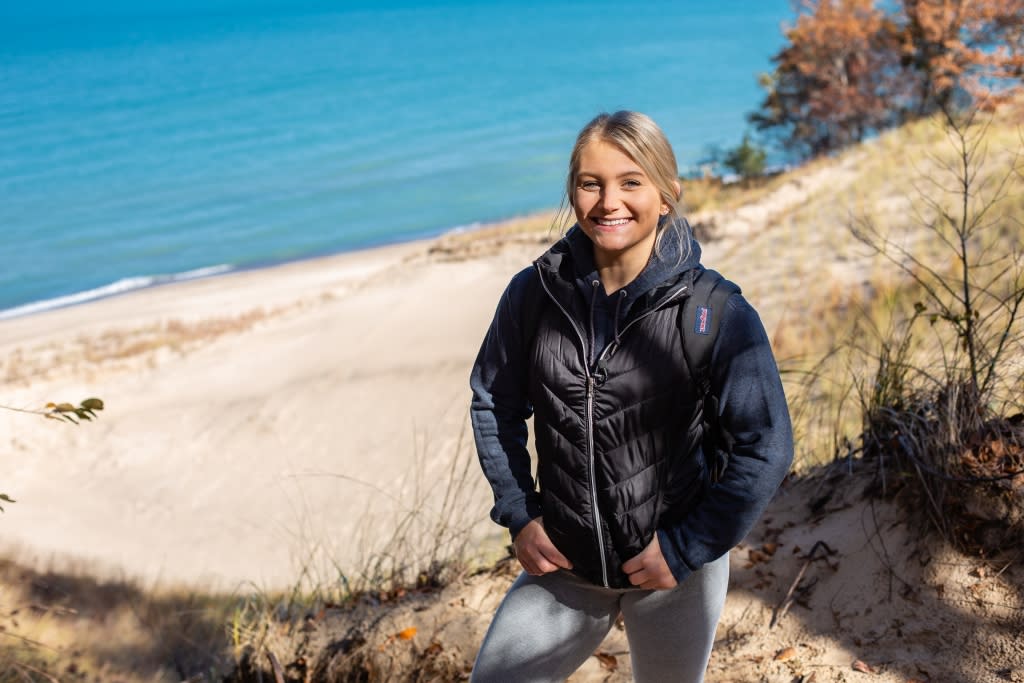 Young woman stands on a sand dune with a view of Lake Michigan in the background.
