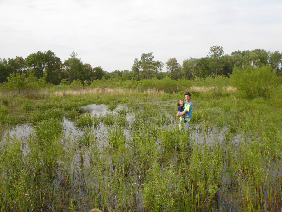 A man holding a young girl while standing in a wetland