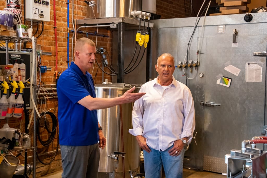 A man in a blue shirt and a man in a pink long sleeve button down shirt stand in a brewery kitchen