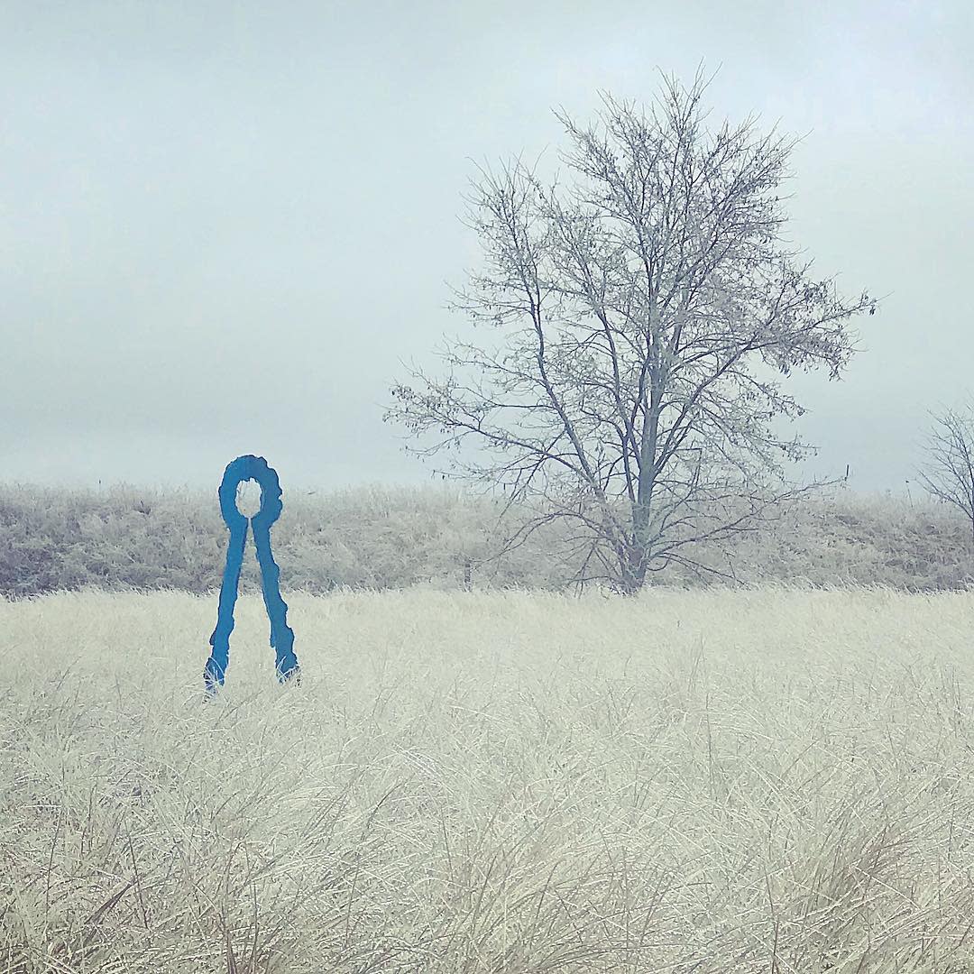 key shaped blue sculpture rises above iced over grass. bare tree stands to one side