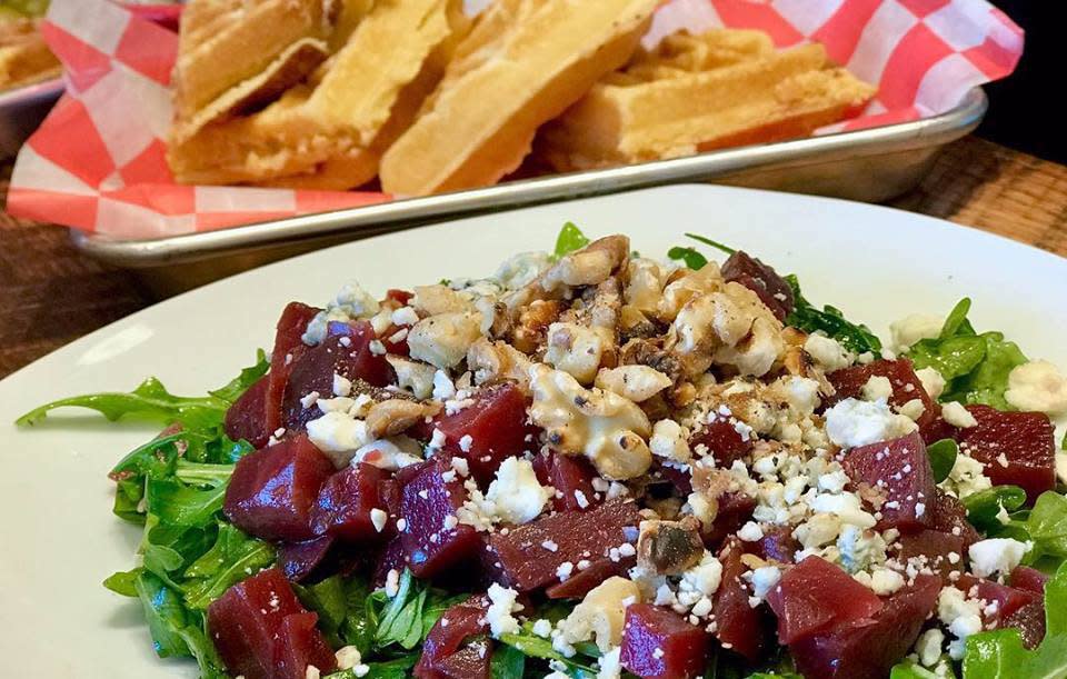 An oval shape white plate with green lettuce on along with diced red beets and feta cheese sprinkled on it. in the background waffles are on a second plate
