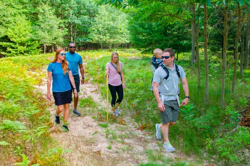 two couples walk along trail flanked by green trees and foliage.