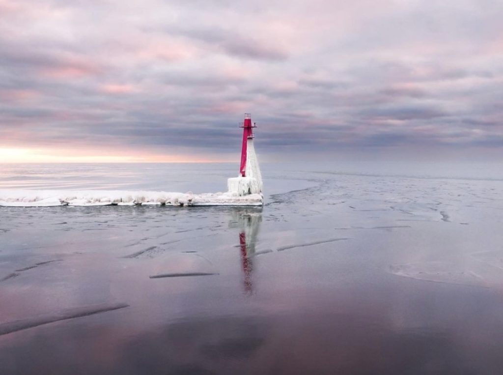 lake michigan light tower on end of snow covered pier set against pink and lavender sunset reflected in frozen water