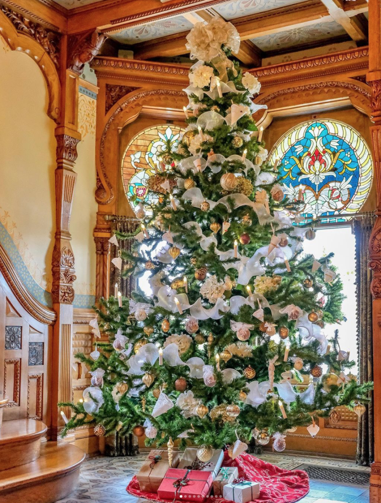 decorated christmas tree sits in front of stained glass windows framed by ornately carved wooden trim