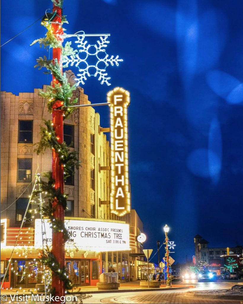 lit marquee on historic theater shines against dark blue evening sky. holiday wrapped pole with large snowflake ornament is in foreground