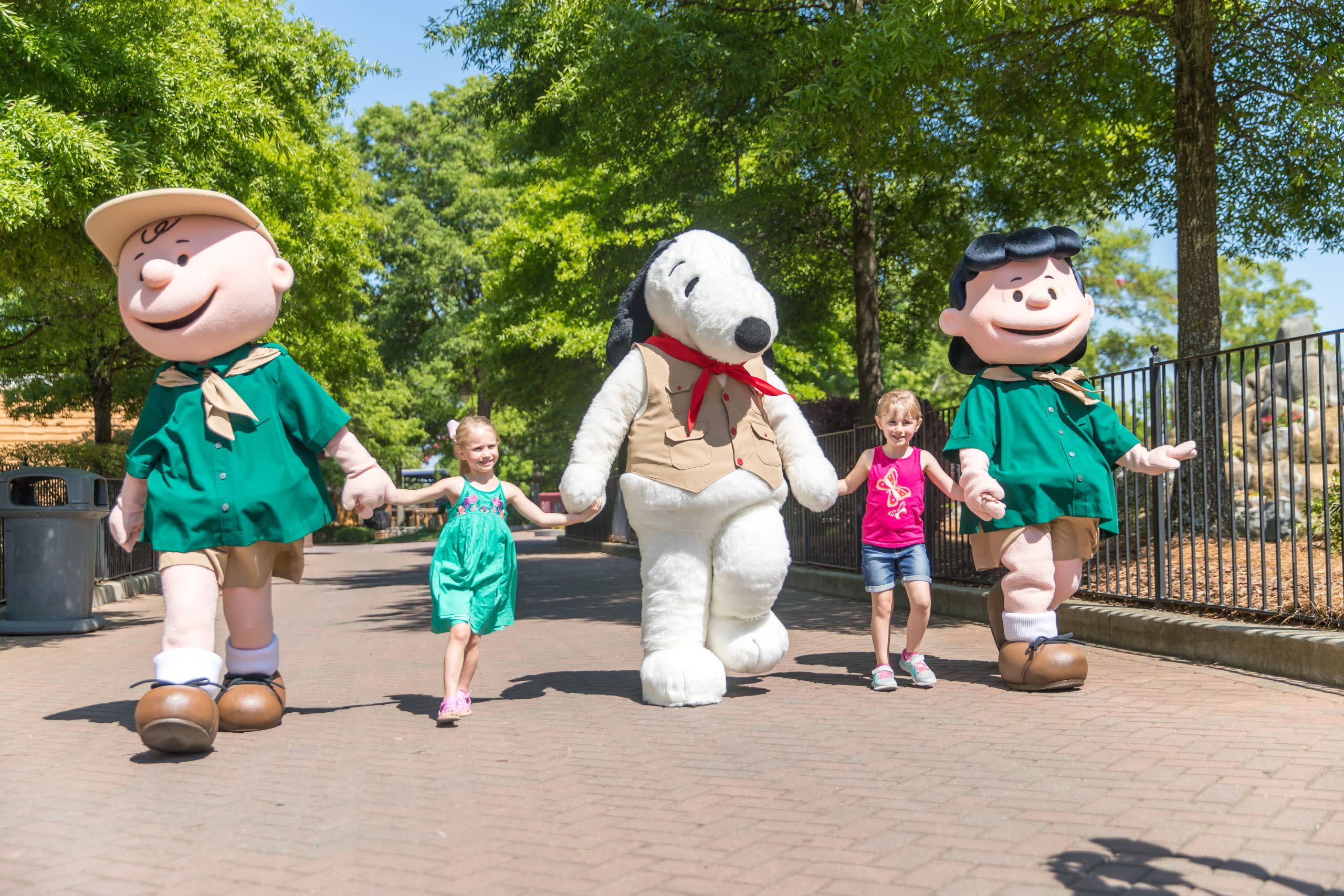 two little girls hold hands with costumed mascots of peanuts characters charlie brown, snoopy and lucy at michigans adventure