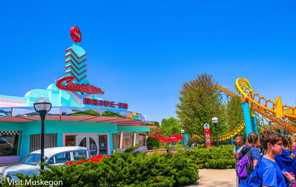 coasters, a bright turquoise 50s style diner at michigans adventure amusement park with yellow rollercoaster to right and red and white vintage car in front