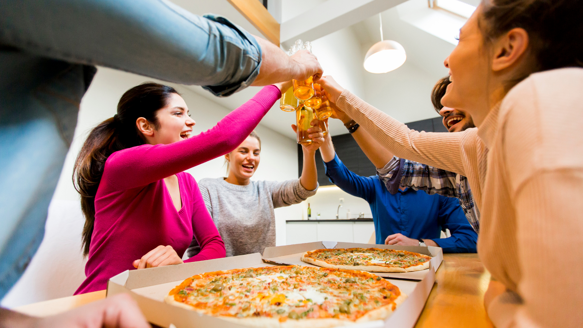 group of young adults toasting with beer glasses over pizzas