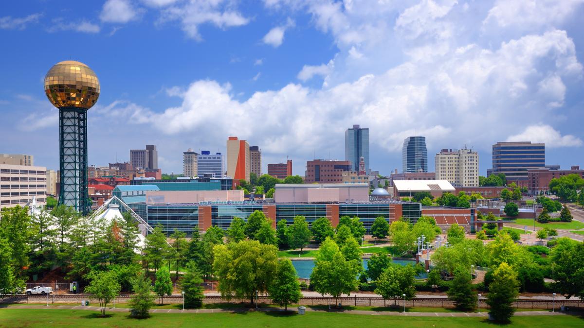 An image of the Sunsphere at the World's Fair Park in Knoxville. There are trees and a pond at the park in the foreground, with a background of downtown Knoxville.