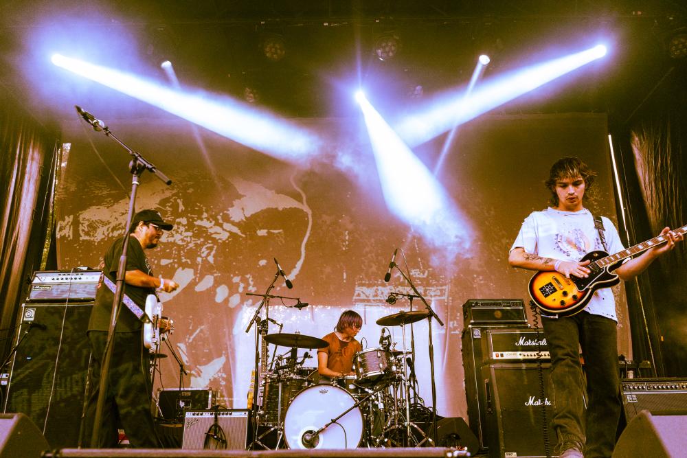 Three members of the Texas shoegaze band Glare perform guitar and drums beneath crossing white stage lights at LEVITATION in Austin