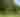A golfer prepares to hit a ball over a stream, surrounded by green trees.