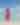 A woman in a pink and red dress walks along the beach