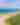 Drone image of a beach that shows the water, beach, and sand dunes from very high. Down the beach, a few cars and a pier are visible.