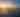 Beautiful sunset over a harbor. The sun is setting behind a bridge of the Americas in the distance, casting a golden light on the water. There are many boats anchored in the harbor, and people can be seen walking along the docks.