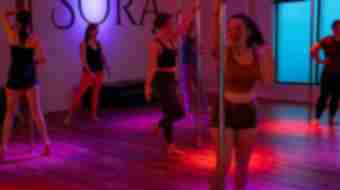 Pink-hued photo of pole exercise class - 6 people are exercising and dancing with poles