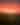 A barn sits on the horizon of a grassy field beneath a vibrant red aurora borealis.