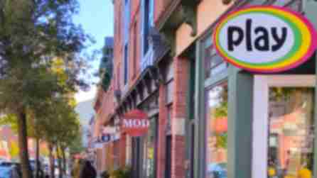 Beacon's Main Street lined with brick buildings and colorful shop signs, including "play" and "MOD." Trees line the sidewalk under a clear blue sky.