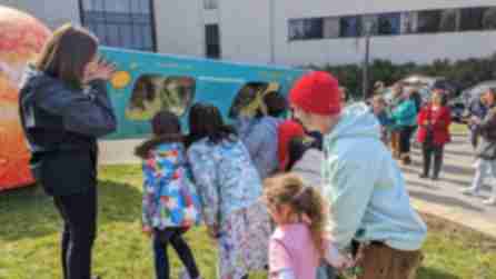 A group of children look through an over-sized pair of solar eclipse glasses at the Rochester Museum & Science Center