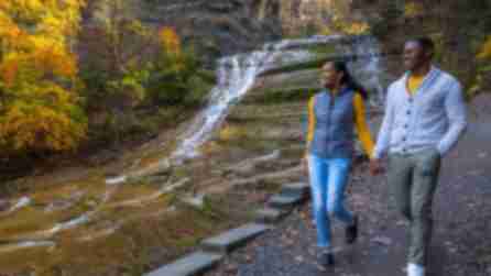 A couple walks along a path near a cascading waterfall at Buttermilk Falls in the Finger Lakes