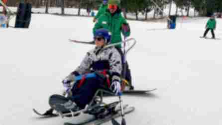 Nikki Walsh of Adapt Fit using adaptive skiing equipment on a snowy slope at Windham Mountain Club, assisted by an Adaptive Sports Foundation instructor in green.