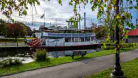 The white and blue trimmed Chautauqua Belle steamboat in the water surrounded by trees turning color for fall