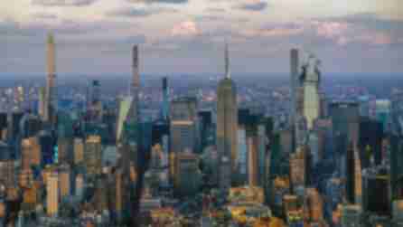 Aerial view of a bustling city skyline at dusk, featuring tall skyscrapers under a partly cloudy sky. Warm light casts shadows, creating a dynamic scene.