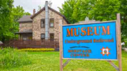 A blue and orange sign of the Museum of the Underground Railroad outside the museum's brick house building