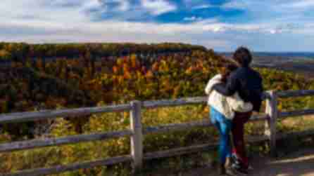 A couple hugging as they look out at mountains decorated in fall foliage in John Boyd Thacher State Park