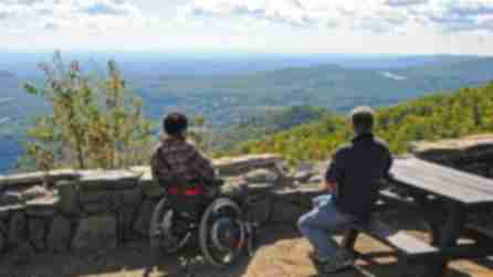 Two people, one in a wheelchair, the other at a picnic table, take in the view from a scenic overlook in New York