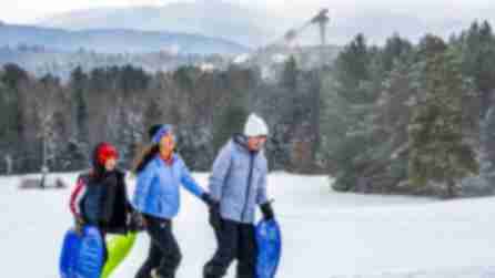 People walking with sleds on snow against backdrop of mountains