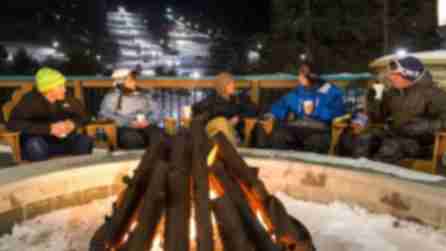 Skiiers sitting around a bonfire with warm beverages