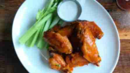 A plate of Buffalo wings with celery and blue cheese sauce