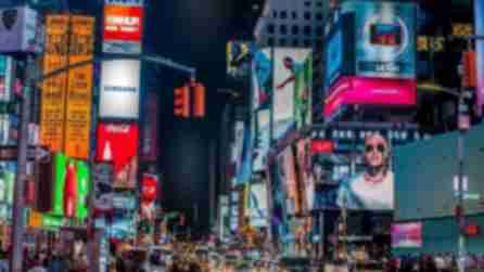 A group of cars waiting at the cross-section of 44th Street and Broadway at night, illuminated by the surrounding billboards on skyscrapers around Broadway and Times Square