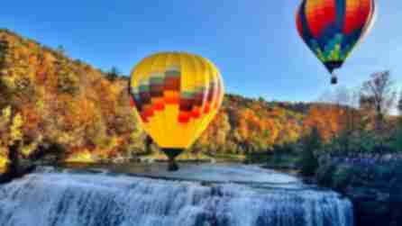 Two brightly-colored hot air balloons float over a waterfall at Letchworth State Park