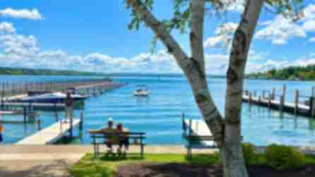 Couple sits on bench overlooking Skaneateles lake, a pier, docked boats, and lush greenery