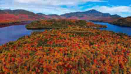 Varying colors of red, orange, yellow, and green trees surround blue lake waters with colorful mountains in the background